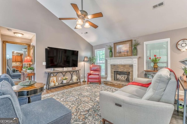 living room with a stone fireplace, a ceiling fan, wood finished floors, high vaulted ceiling, and baseboards