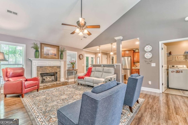 living room featuring washer / dryer, ceiling fan, light wood-style flooring, baseboards, and a stone fireplace