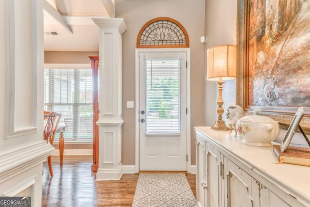 doorway with decorative columns, light wood finished floors, and plenty of natural light