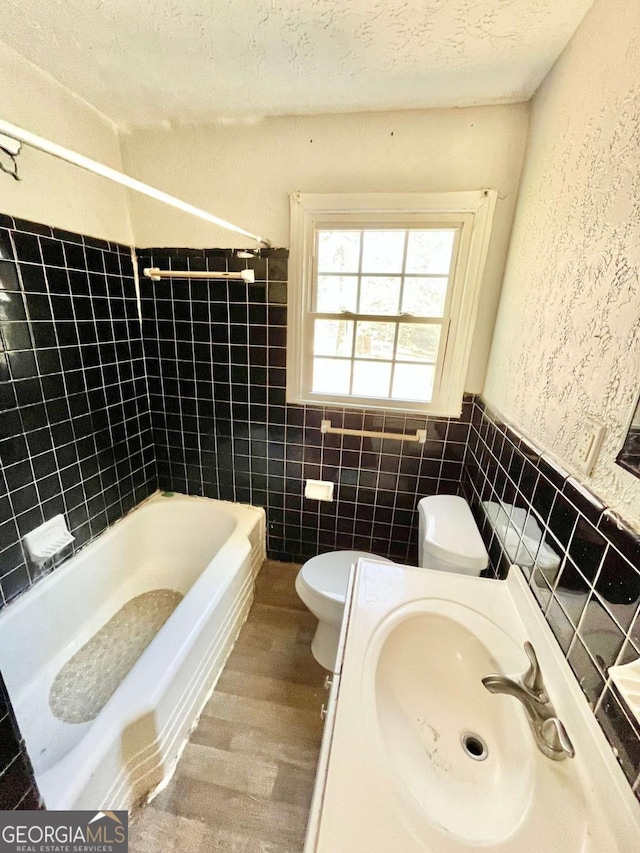 bathroom featuring wood finished floors, a sink, toilet, tile walls, and a wainscoted wall
