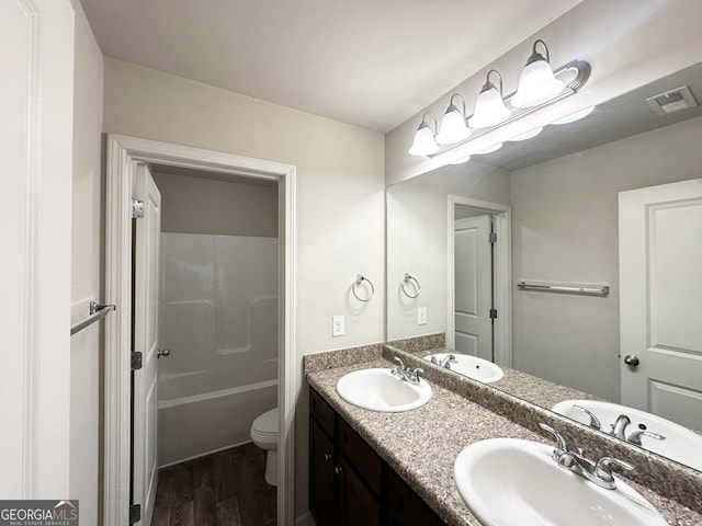 bathroom featuring wood finished floors, toilet, double vanity, and bathtub / shower combination