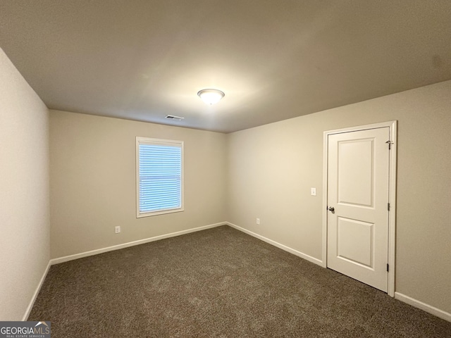 unfurnished room featuring dark colored carpet and baseboards