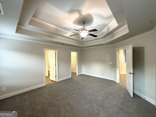 unfurnished bedroom with a raised ceiling, ornamental molding, dark colored carpet, a spacious closet, and baseboards