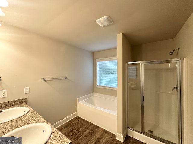 bathroom featuring a shower stall, wood finished floors, a bath, baseboards, and double vanity