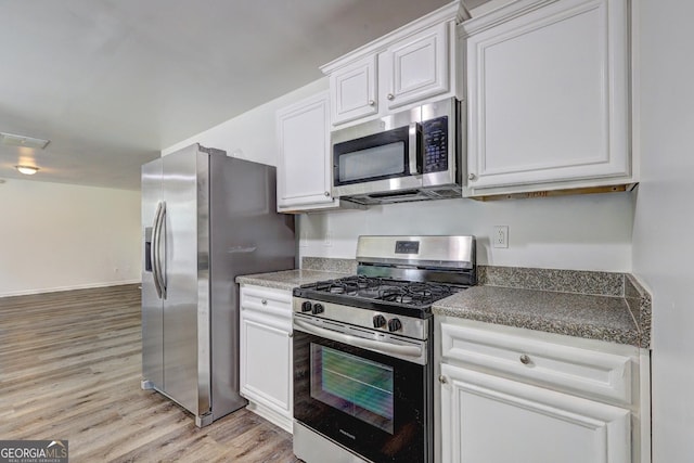 kitchen with appliances with stainless steel finishes, light wood-style flooring, white cabinetry, and dark countertops