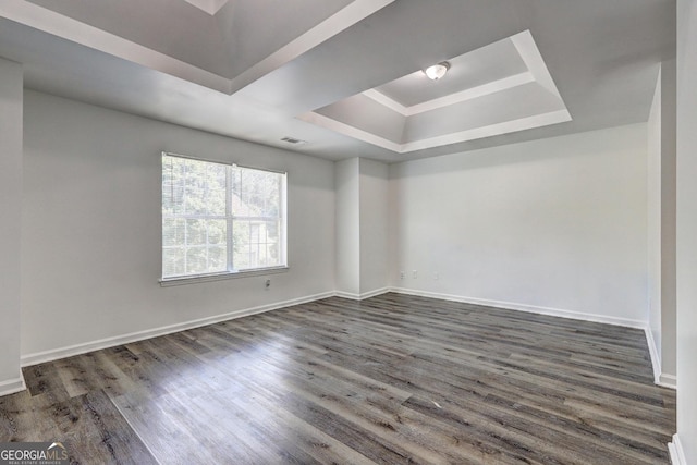 empty room with a tray ceiling, wood finished floors, and baseboards