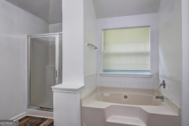 bathroom with a stall shower, a bath, wood finished floors, and vaulted ceiling
