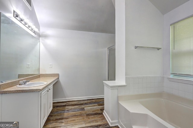 full bathroom with wood finished floors, a garden tub, vanity, and vaulted ceiling