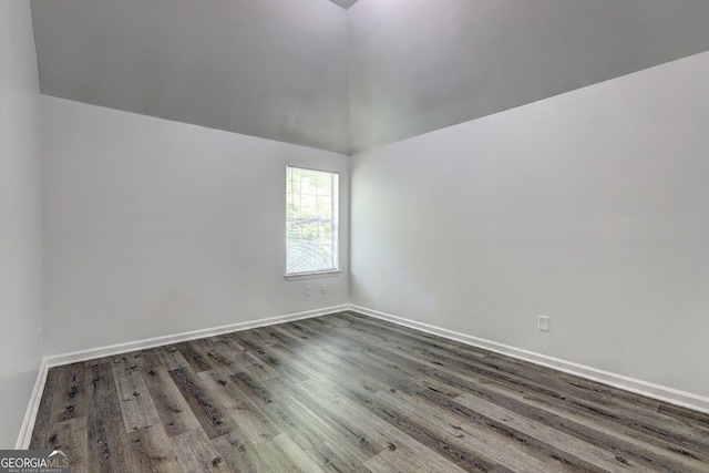 empty room featuring dark wood-style flooring, vaulted ceiling, and baseboards
