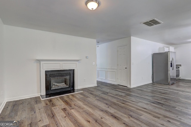 unfurnished living room with wood finished floors, a fireplace with raised hearth, and baseboards