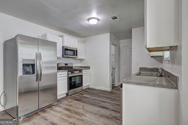 kitchen featuring stainless steel appliances, a sink, light wood-style floors, white cabinets, and baseboards