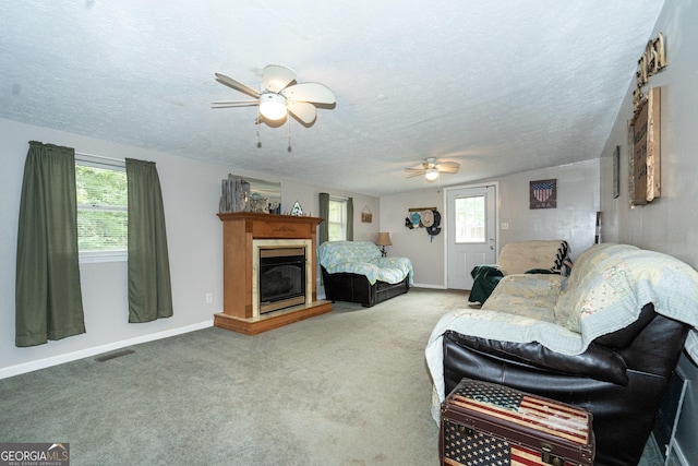 carpeted living area featuring ceiling fan, a textured ceiling, baseboards, and a glass covered fireplace
