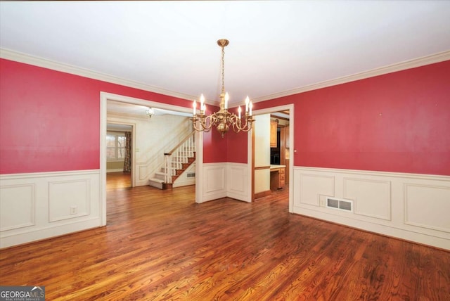 unfurnished dining area featuring a chandelier, stairs, a wainscoted wall, crown molding, and wood finished floors