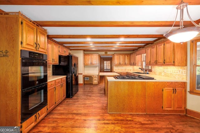 kitchen featuring black appliances, wood finished floors, light countertops, and beamed ceiling
