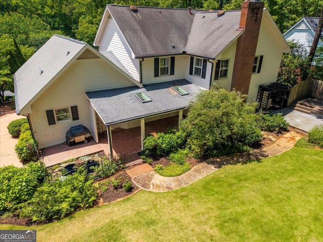 back of property featuring a chimney, a lawn, roof with shingles, and a patio