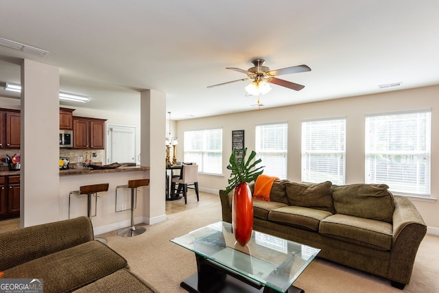 living room with light carpet, a ceiling fan, baseboards, and a chandelier