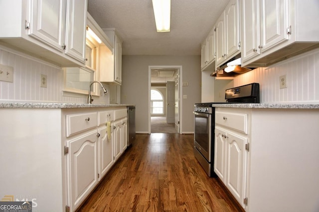 kitchen with appliances with stainless steel finishes, dark wood-type flooring, white cabinets, a sink, and under cabinet range hood