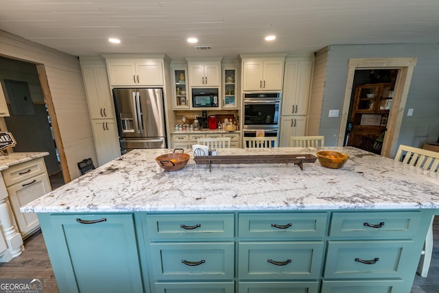 kitchen with appliances with stainless steel finishes, a center island, dark wood-type flooring, light stone countertops, and glass insert cabinets