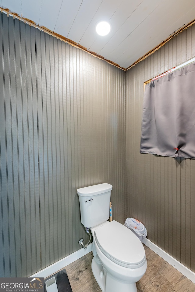 bathroom featuring wood finished floors, toilet, baseboards, and wood walls