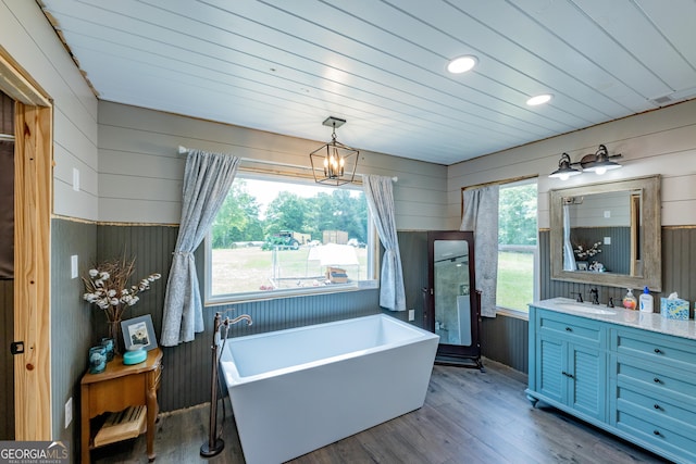 full bath with wooden walls, wood finished floors, a chandelier, a freestanding tub, and vanity