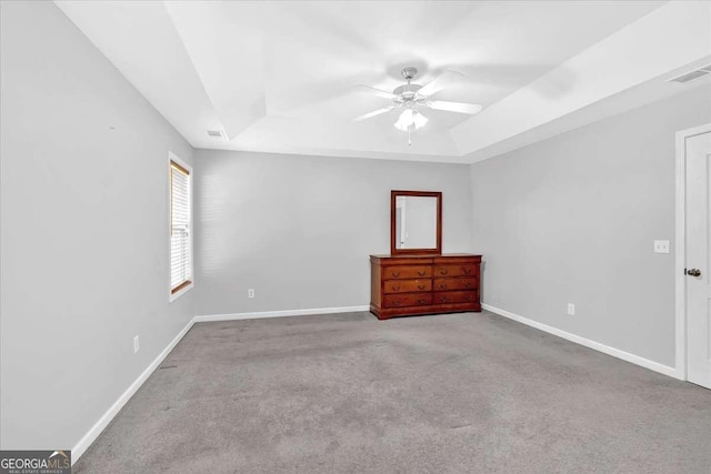 carpeted spare room with a raised ceiling, a ceiling fan, and baseboards