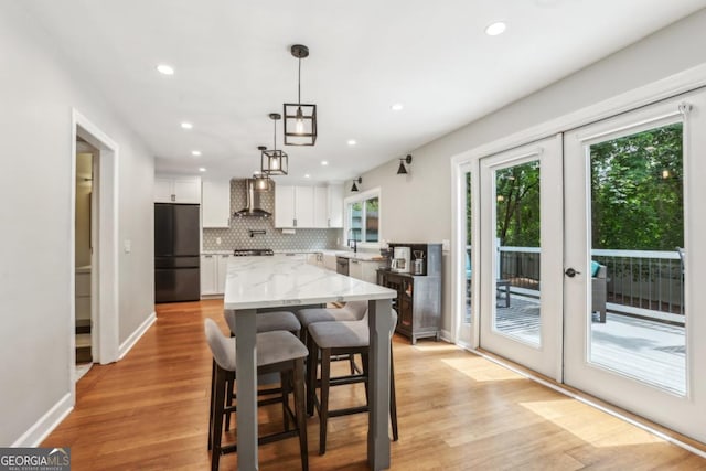kitchen featuring freestanding refrigerator, wall chimney exhaust hood, white cabinets, decorative backsplash, and recessed lighting