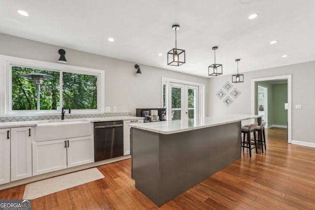kitchen featuring dishwasher, a sink, recessed lighting, white cabinets, and light stone countertops