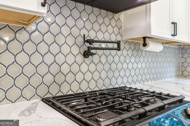 kitchen with stovetop, light stone countertops, white cabinetry, backsplash, and exhaust hood
