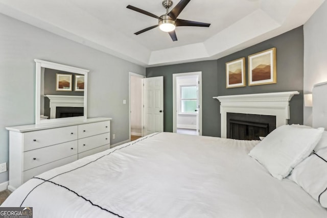 bedroom featuring a fireplace, a tray ceiling, baseboards, connected bathroom, and a ceiling fan