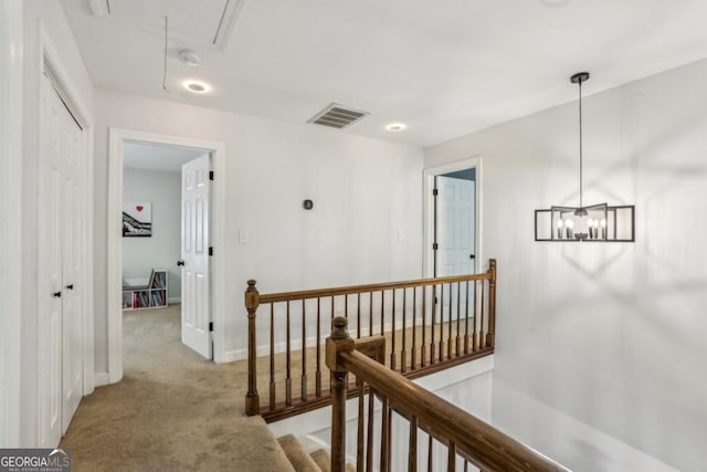 corridor featuring an upstairs landing, attic access, light colored carpet, baseboards, and a chandelier