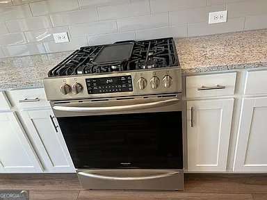 1616 Avery Way, Tucker, GA 30084 - kitchen view of gas stove, white cabinetry, light stone counters, and backsplash