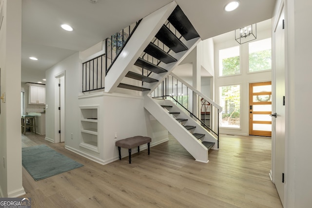 staircase with wood finished floors, recessed lighting, baseboards, a chandelier, and a towering ceiling