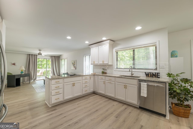 kitchen featuring dishwasher, a sink, a peninsula, white cabinetry, and plenty of natural light