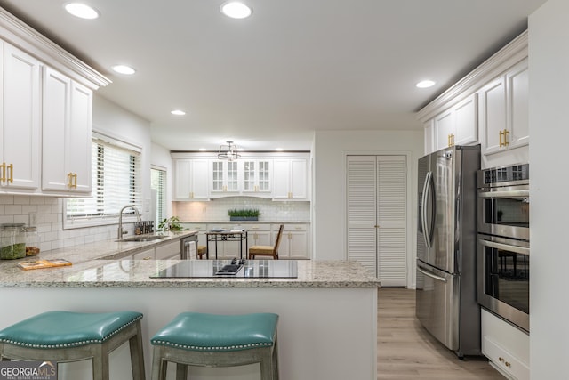 kitchen featuring appliances with stainless steel finishes, a sink, a peninsula, white cabinets, and recessed lighting