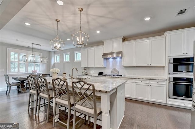 kitchen with a sink, double oven, a chandelier, under cabinet range hood, and dark wood-type flooring