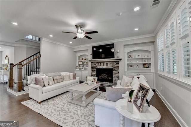 living room with wood finished floors, stairway, ceiling fan, crown molding, and a stone fireplace