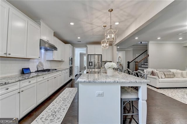 kitchen with a sink, under cabinet range hood, a chandelier, stainless steel appliances, and a breakfast bar