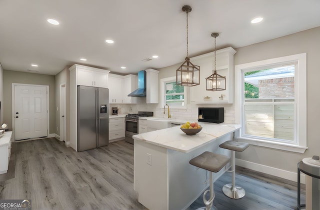 3275 Dodson Dr, East Point, GA 30344 - kitchen featuring appliances with stainless steel finishes, wall chimney exhaust hood, a peninsula, baseboards, and white cabinetry