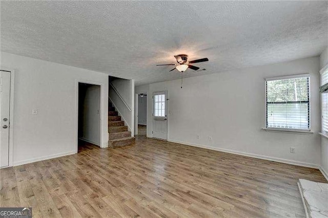 unfurnished living room featuring a textured ceiling, healthy amount of natural light, a ceiling fan, light wood finished floors, and stairway