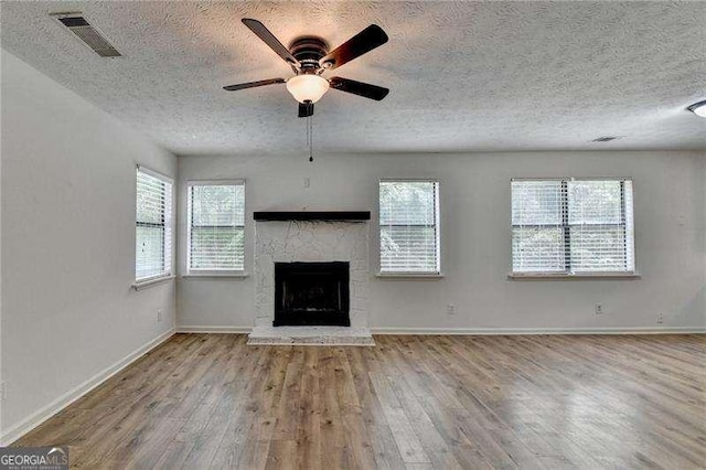unfurnished living room with a textured ceiling, wood finished floors, a ceiling fan, a stone fireplace, and baseboards