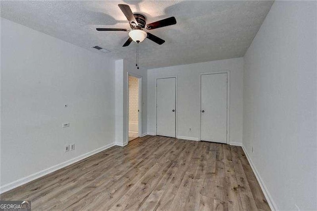unfurnished bedroom featuring wood finished floors, multiple closets, a textured ceiling, baseboards, and a ceiling fan
