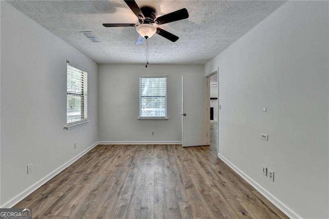 unfurnished room with a textured ceiling, wood finished floors, a ceiling fan, and baseboards