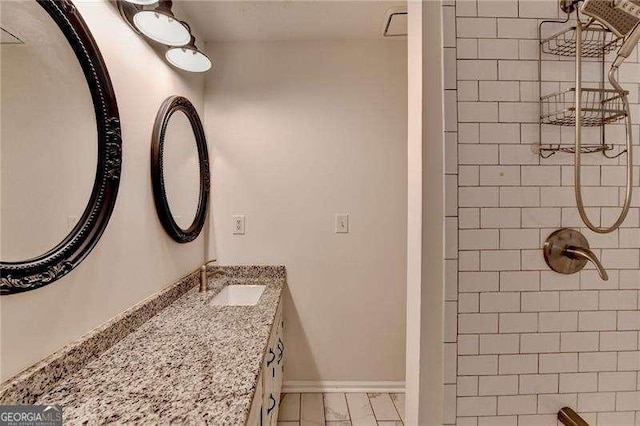 full bathroom with tiled shower, vanity, and baseboards