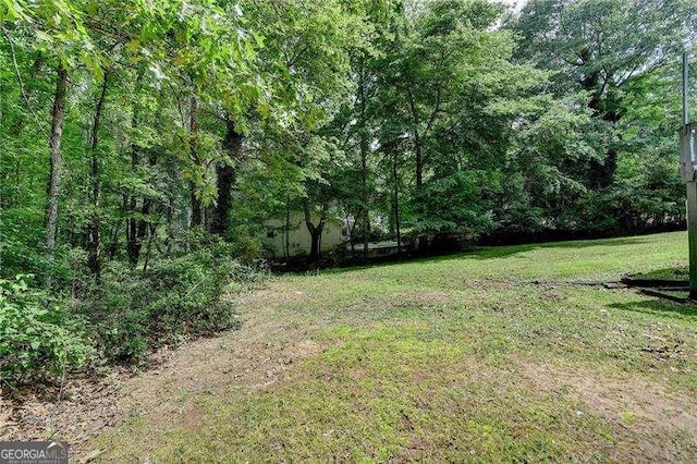 view of green lawn featuring a forest view