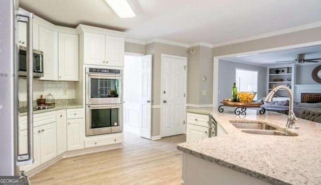 kitchen featuring appliances with stainless steel finishes, a sink, white cabinets, crown molding, and light stone counters