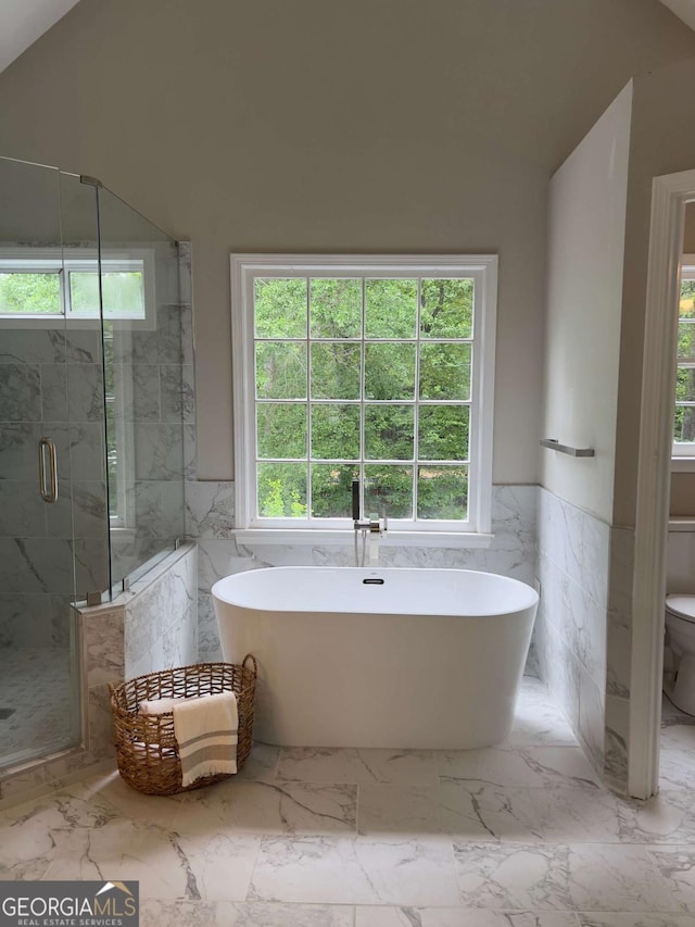bathroom with tile walls, plenty of natural light, a marble finish shower, lofted ceiling, and wainscoting