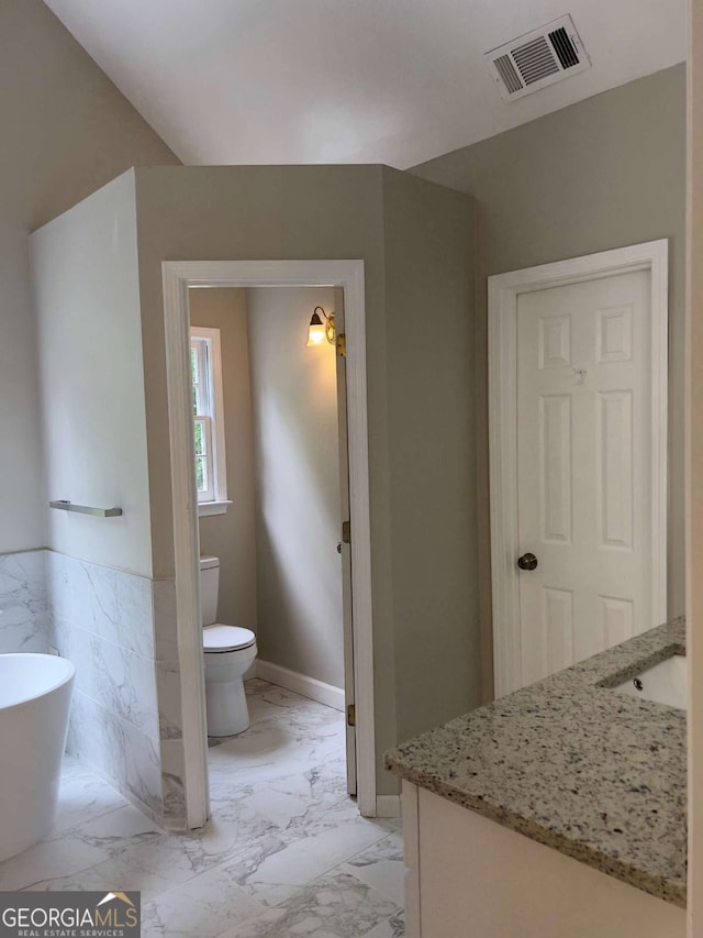 full bath featuring vanity, toilet, a freestanding bath, marble finish flooring, and baseboards