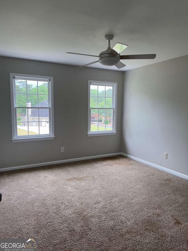 carpeted spare room with a ceiling fan and baseboards