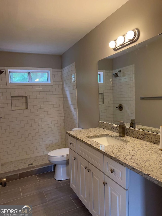 bathroom with tiled shower, toilet, vanity, and wood tiled floors