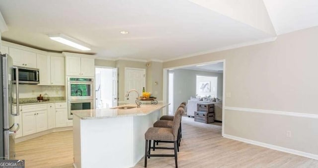 kitchen with a sink, stainless steel appliances, light wood-style floors, a breakfast bar area, and backsplash